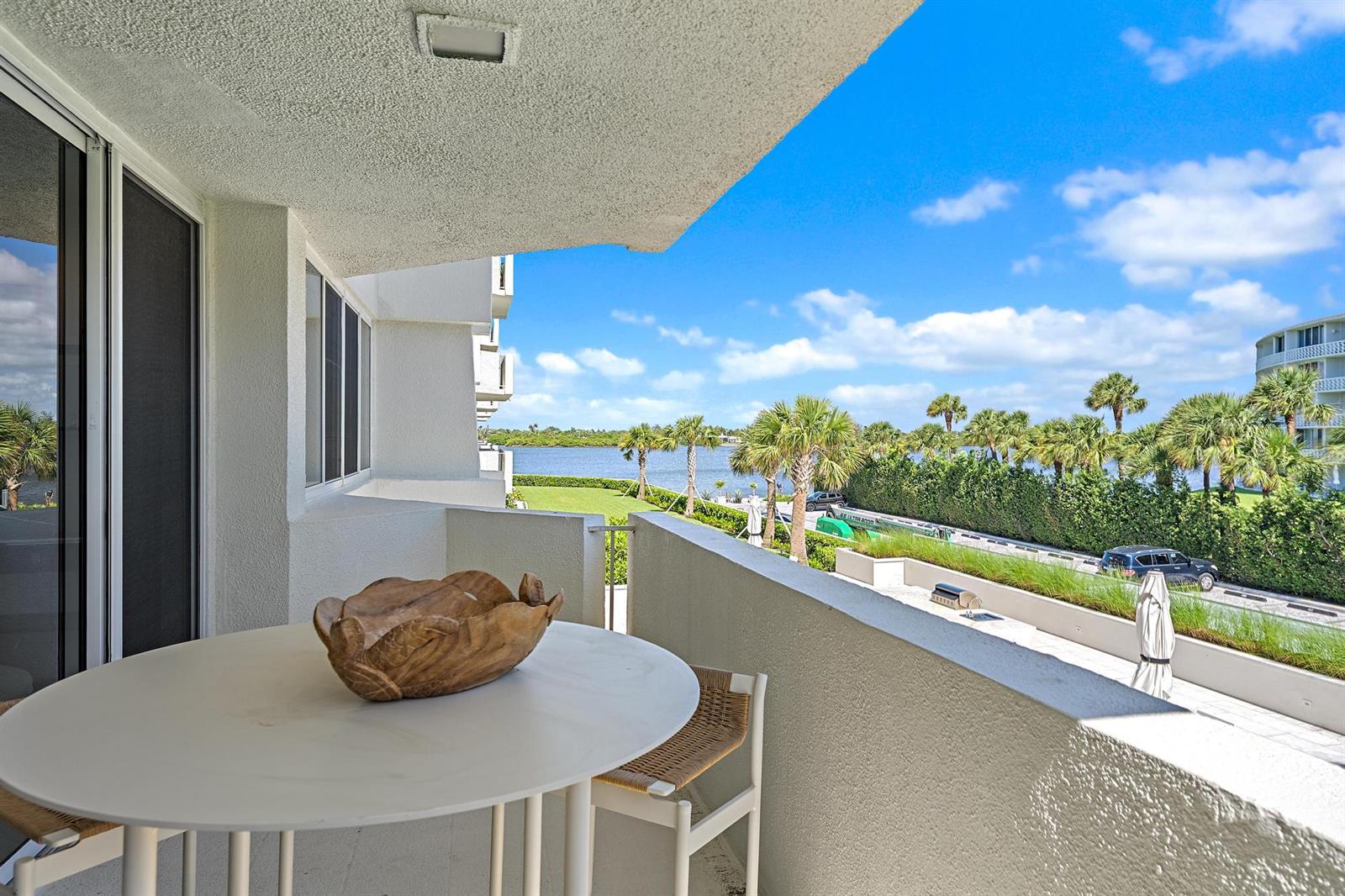 A balcony with a round table, wooden bowl, and chairs overlooks a waterfront landscape — 2773 S Ocean Boulevard # 209, Palm Beach FL 33480, PALM BEACH, FL
