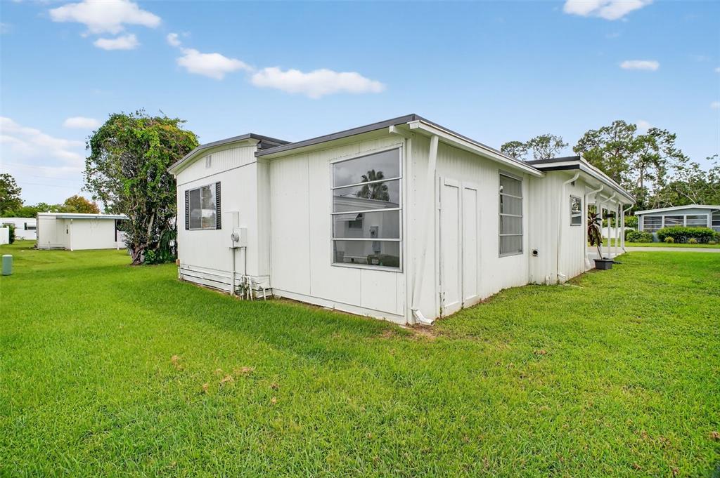 The exterior of a white mobile home features a large window and a grassy yard — 227 PARADISE S, LEESBURG, FL