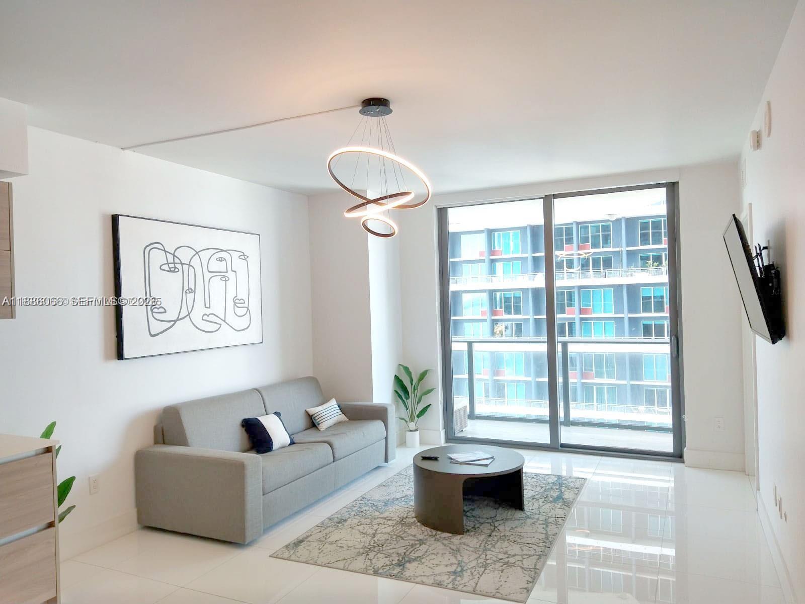 A living room features a grey sofa, a circular coffee table, and a modern light fixture — 1300 S Miami Ave # 2208, Miami FL 33130, MIAMI, FL
