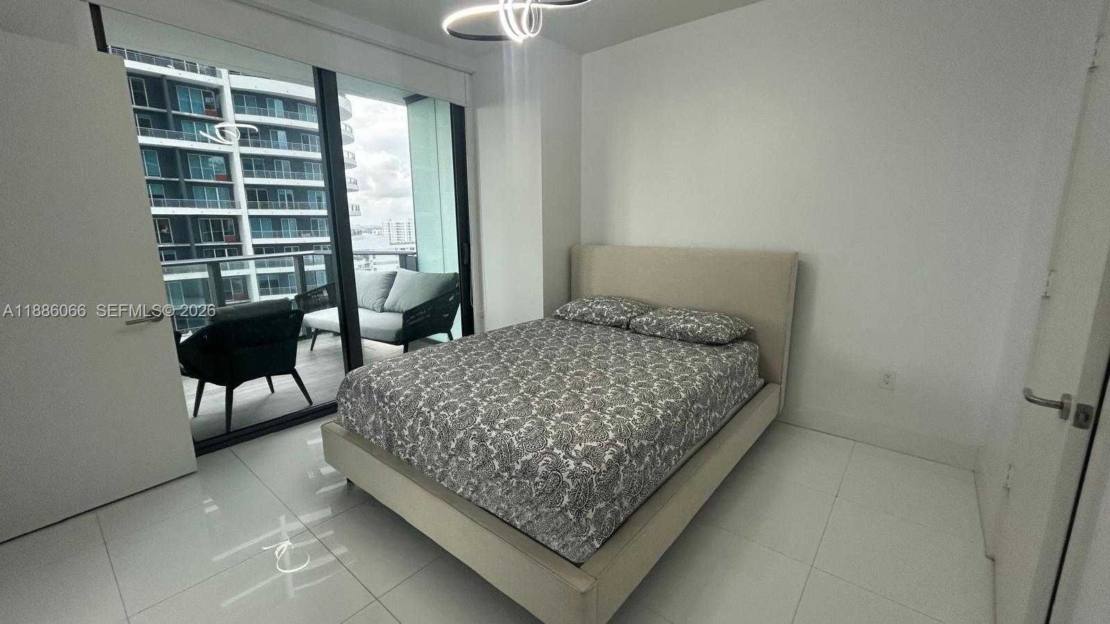 A bedroom with a bed, white tile floors, and a balcony overlooking a city building — 1300 S Miami Ave # 2208, Miami FL 33130, MIAMI, FL