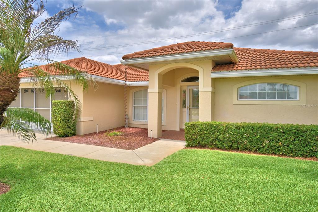 A single-story house with a terracotta tile roof, beige stucco walls, and a covered entryway — 142 MORNING GLORY CIRCLE, WINTER HAVEN, FL