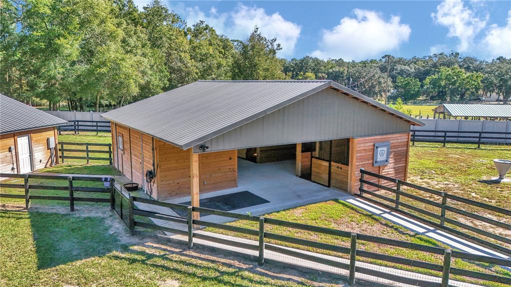 A wooden horse barn with a metal roof stands in a fenced grassy pasture — 521 NW 80TH AVENUE, OCALA, FL