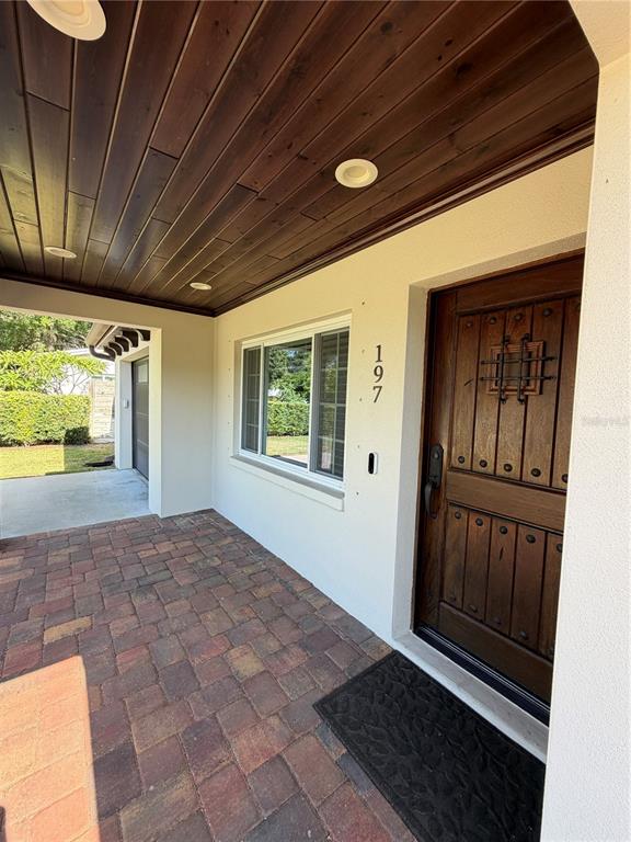 A covered entryway features a wood-paneled ceiling, a wooden door, and a brick paver floor — 197 IRWIN STREET W, SAFETY HARBOR, FL