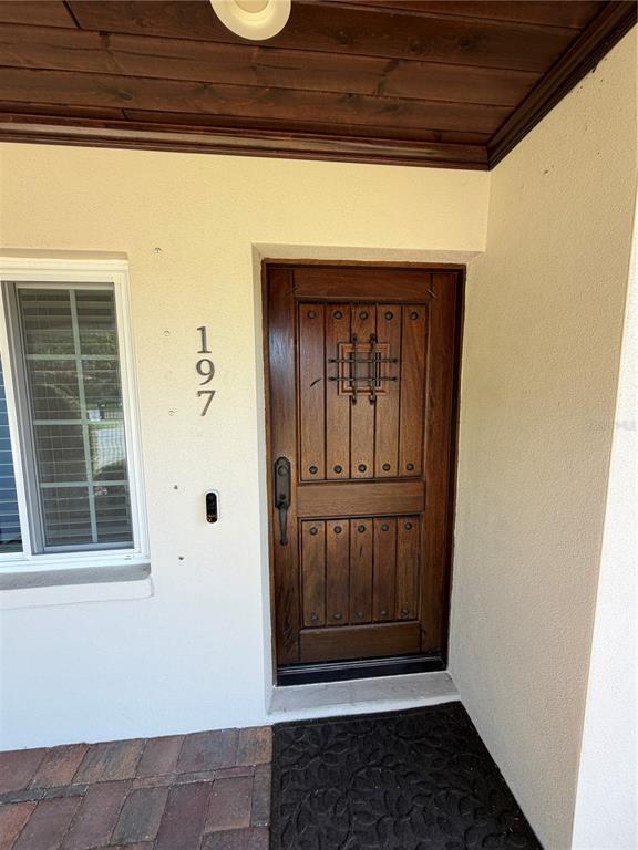 A wooden front door with a metal grate window sits beside a window and house numbers — 197 IRWIN STREET W, SAFETY HARBOR, FL