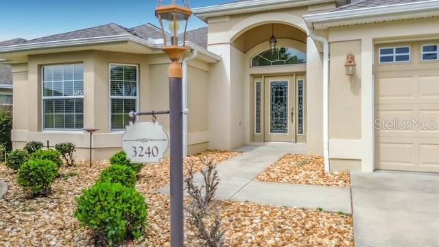 A beige house exterior features a front entrance, a garage, and a decorative address post — 3240 LAFAYETTE STREET, THE VILLAGES, FL