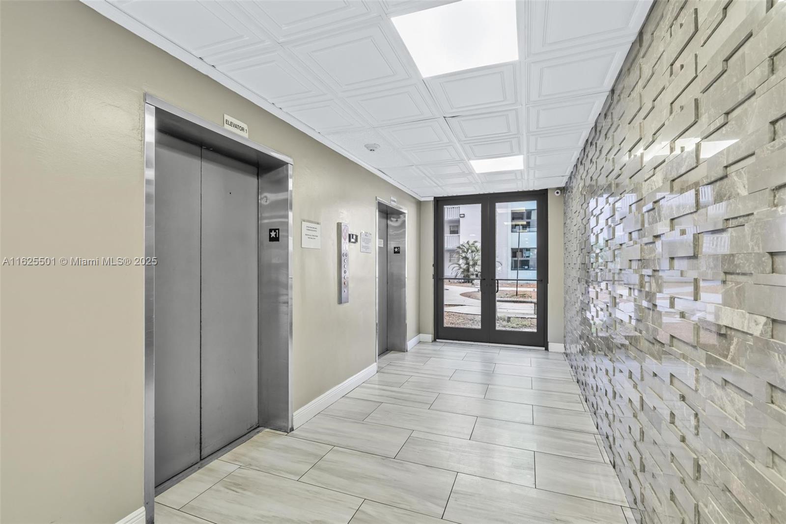 An elevator lobby features two metal elevator doors, a textured stone wall, and tile flooring — 15600 NW 7th Ave # 306, Miami FL 33169, MIAMI, FL