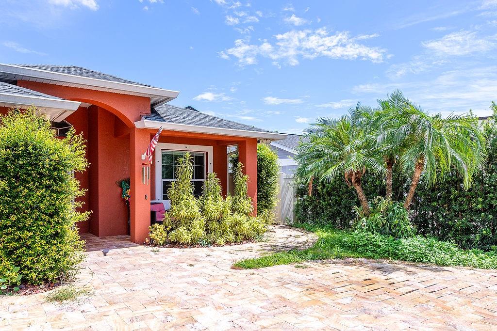 A terracotta-colored house exterior features a paved walkway, lush landscaping, and a palm tree — 4907 CARLYLE ROAD, TAMPA, FL