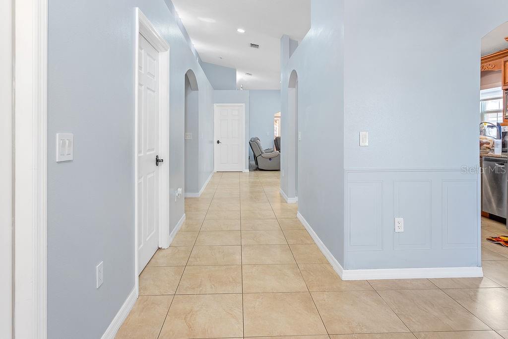 A hallway with light blue walls, tile flooring, and white doors leads to a living area — 4907 CARLYLE ROAD, TAMPA, FL