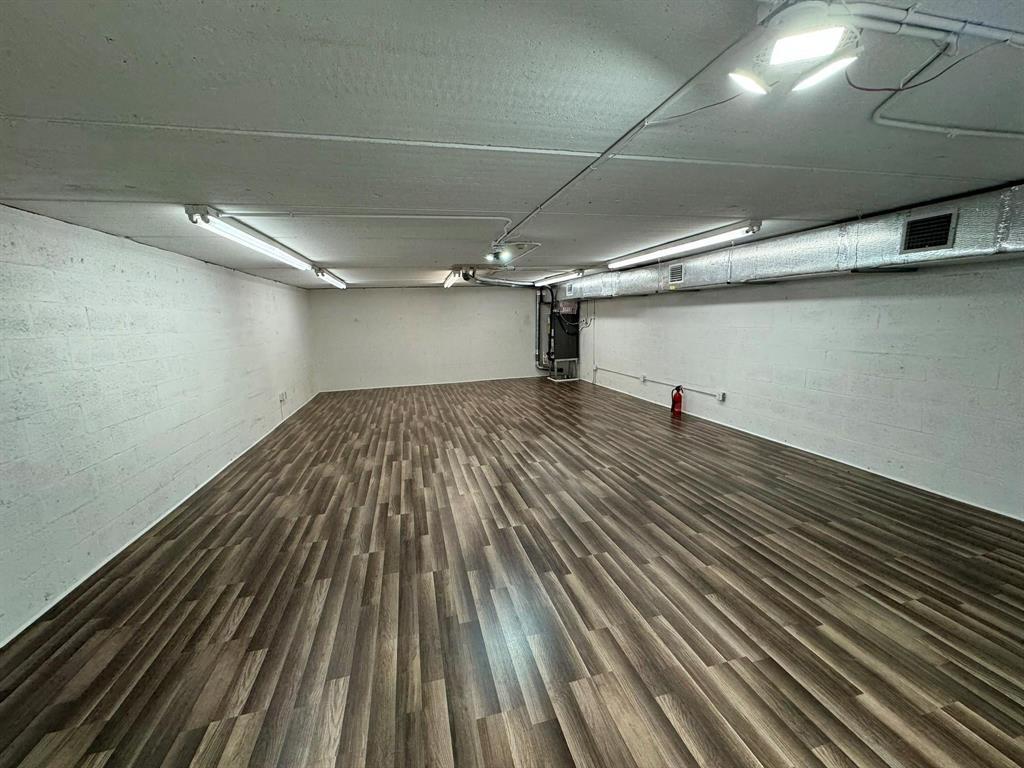 An empty basement room features white painted block walls, wood-look flooring, and exposed ceiling lights — 1773 Blount Road # 313, Pompano Beach FL 33069, POMPANO BEACH, FL