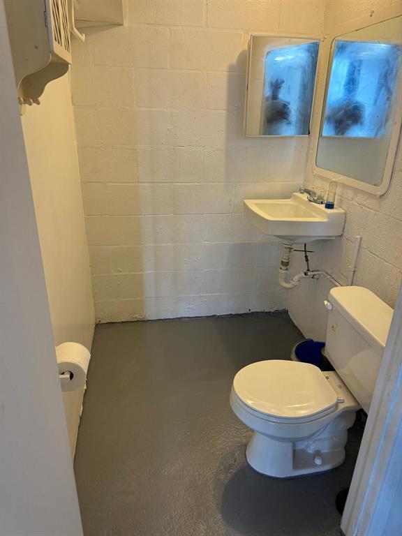 A small bathroom with a white wall-mounted sink, a toilet, and painted concrete walls — 1773 Blount Road # 313, Pompano Beach FL 33069, POMPANO BEACH, FL