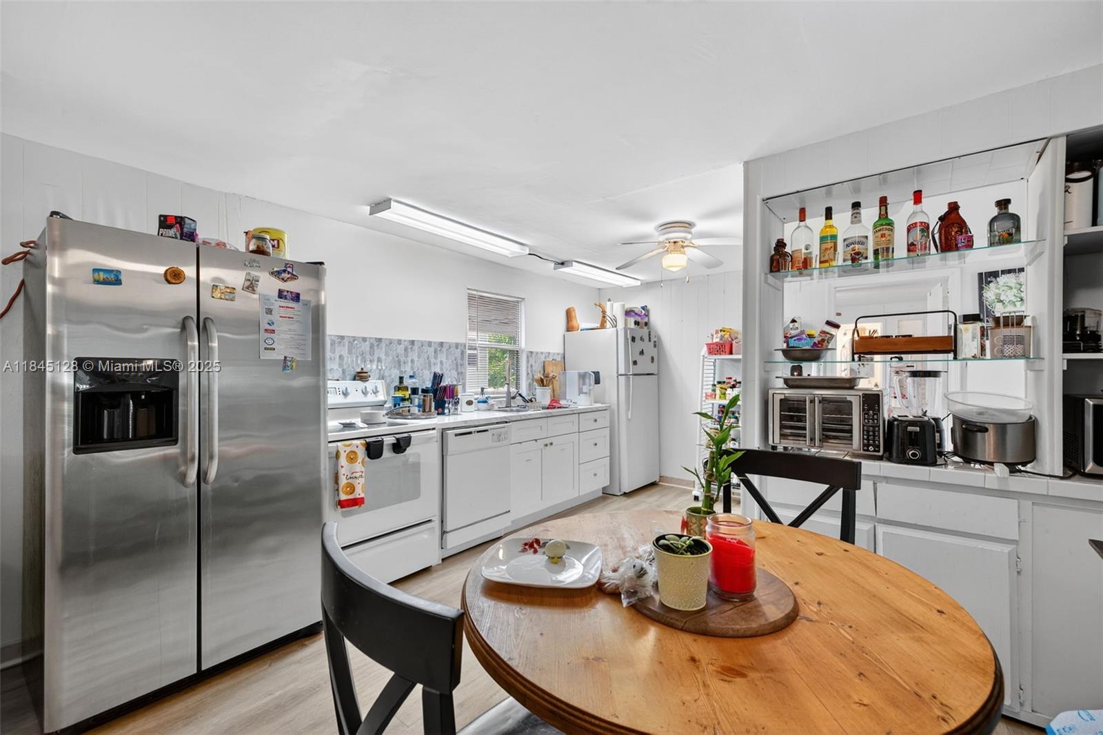A kitchen features white cabinets, stainless steel appliances, and a round wooden dining table — 2430 SW 53rd St, Dania Beach FL 33312, DANIA BEACH, FL