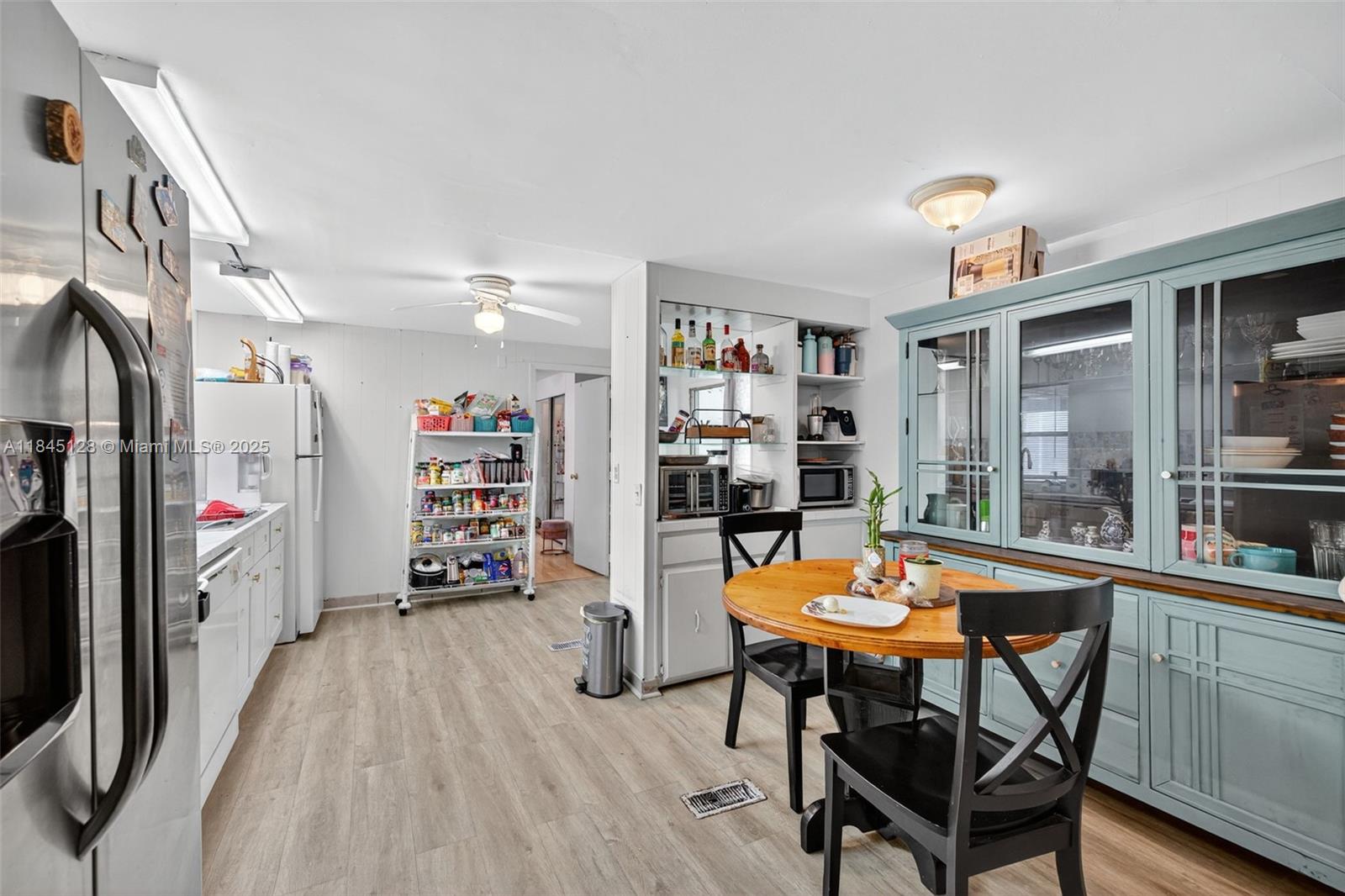 A kitchen and dining area features white cabinets, a blue hutch, and light wood flooring — 2430 SW 53rd St, Dania Beach FL 33312, DANIA BEACH, FL