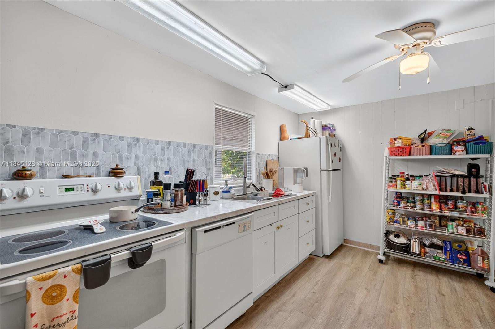 A kitchen features white cabinets, a white stove, a dishwasher, a refrigerator, and a wire shelving unit — 2430 SW 53rd St, Dania Beach FL 33312, DANIA BEACH, FL