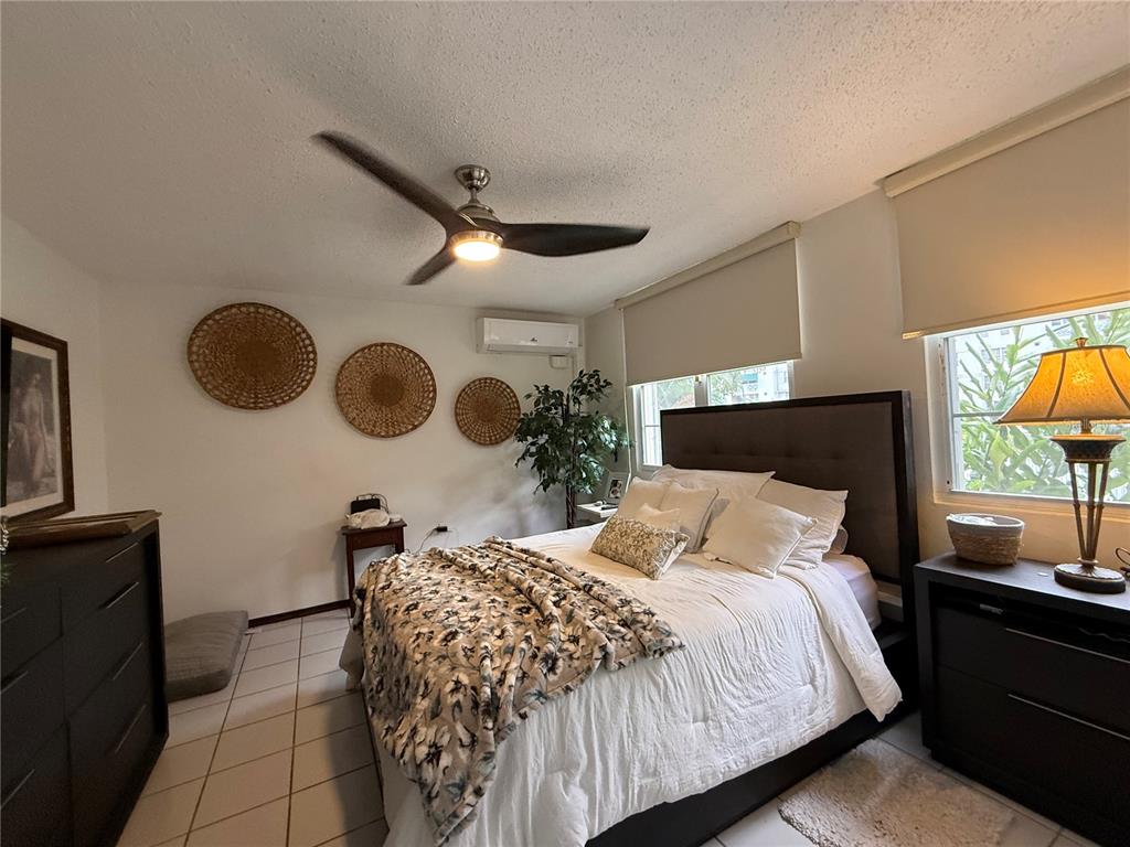 A bedroom features a queen bed, dark wood furniture, tile flooring, and woven wall decor — 57 LOPATEGUI UNIT BB-2, GUAYNABO, PR