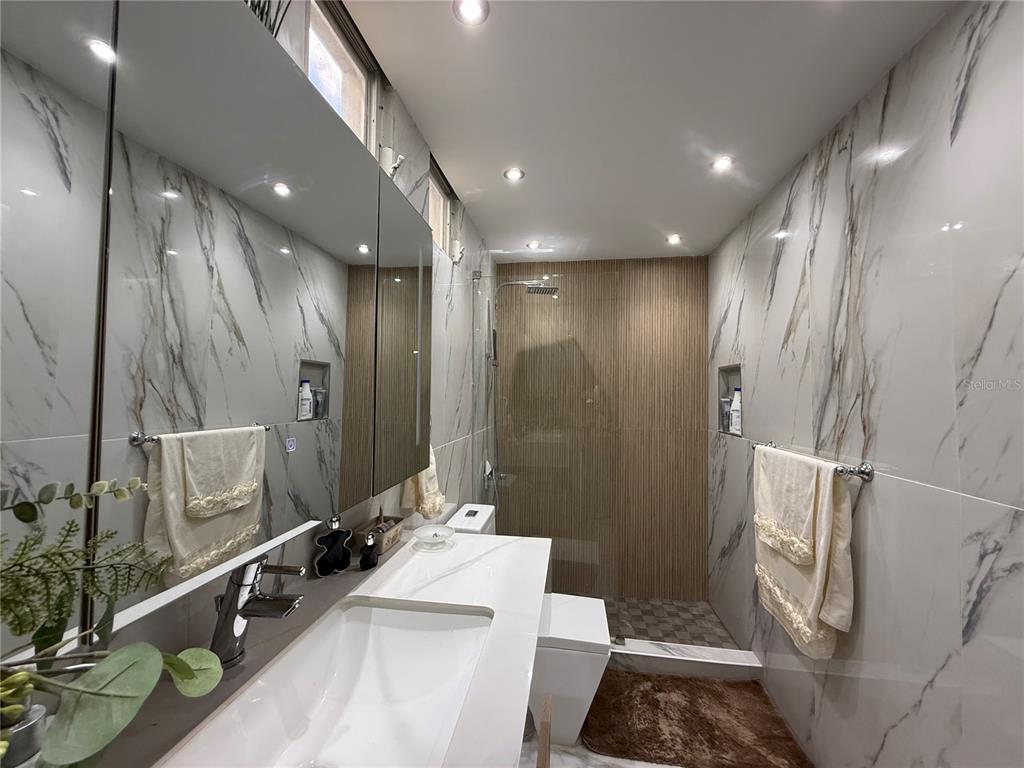A modern bathroom features marble-look wall tiles, a white vanity, and a glass-enclosed walk-in shower — 57 LOPATEGUI UNIT BB-2, GUAYNABO, PR