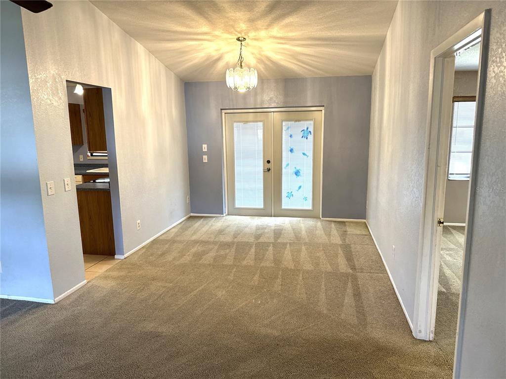 A dining room features beige carpeting, light blue walls, a chandelier, and glass-paned double doors — 2089 WINNINGWAY STREET, PORT CHARLOTTE, FL