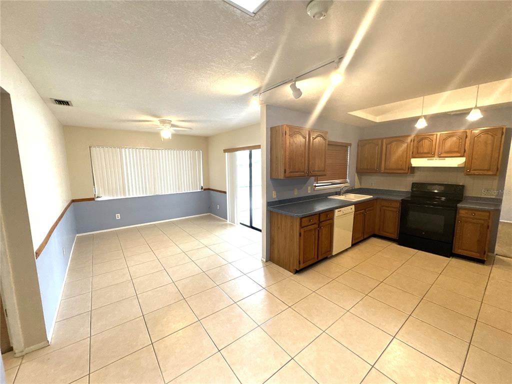 A kitchen with wood cabinets and tile floors opens into a dining area with blinds — 2089 WINNINGWAY STREET, PORT CHARLOTTE, FL