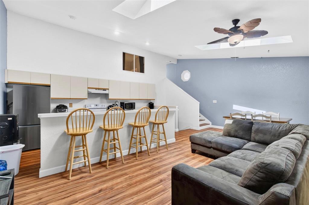 A kitchen features light-colored cabinets, white countertops, a breakfast bar with stools, and wood-look flooring — 6389 93RD TERRACE N UNIT 4706, PINELLAS PARK, FL