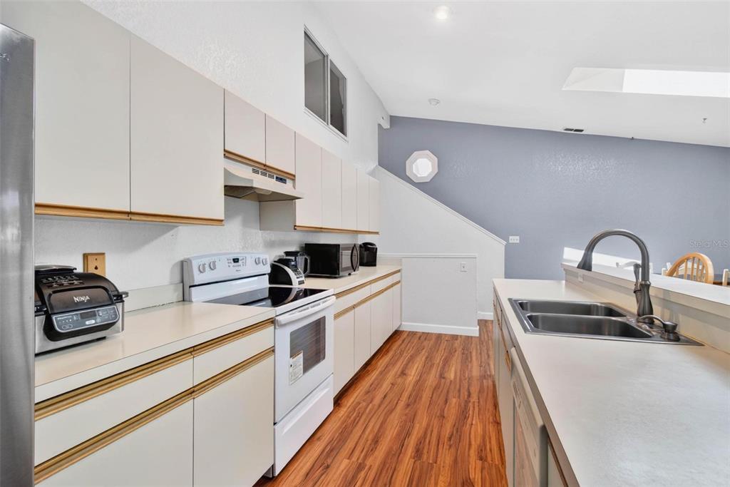 A kitchen features white cabinets, laminate countertops, stainless steel appliances, and wood-look flooring — 6389 93RD TERRACE N UNIT 4706, PINELLAS PARK, FL