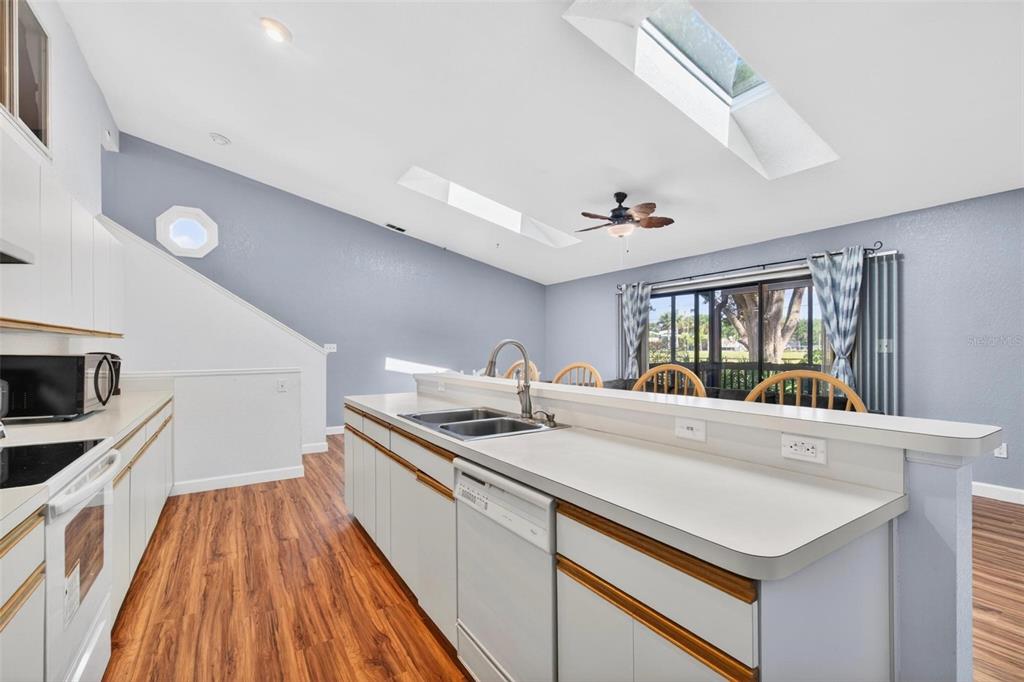 A kitchen with white cabinets and a breakfast bar overlooks a dining area with skylights — 6389 93RD TERRACE N UNIT 4706, PINELLAS PARK, FL