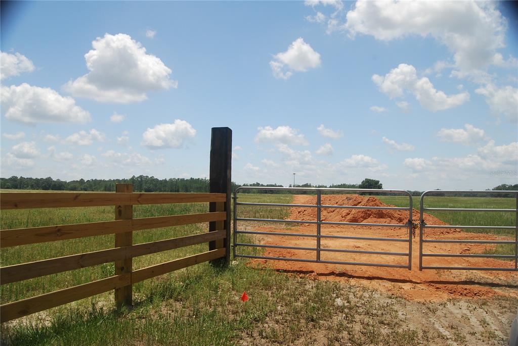 A metal gate and wooden fence enclose a grassy field with a pile of dirt — LAKE ERIE ROAD, CLERMONT, FL