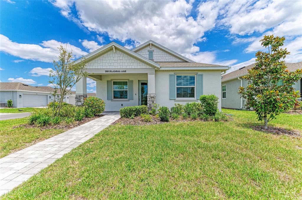 A single-story house with a light-colored stucco exterior, stone accents, and a paved walkway — 1989 SPLASHRAIL LANE, SARASOTA, FL