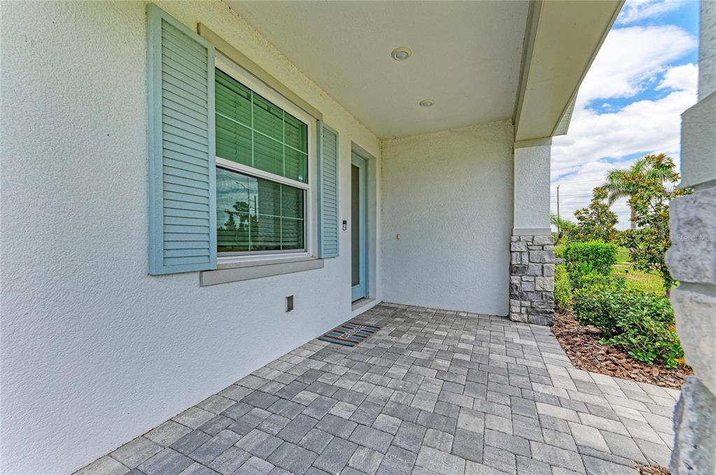 A covered front porch features light-colored pavers, a window with blue shutters, and stone accents — 1989 SPLASHRAIL LANE, SARASOTA, FL
