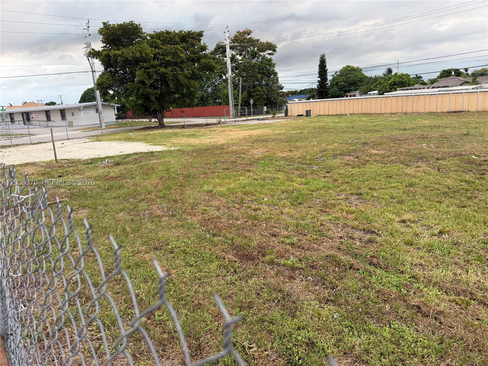 A fenced, grassy vacant lot with a large tree and nearby buildings under a cloudy sky — 291 W 49th St, Hialeah FL 33012, HIALEAH, FL