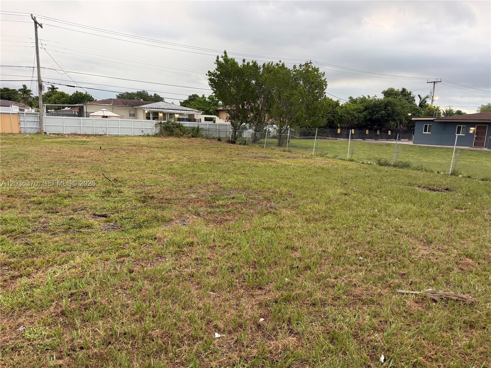 A vacant, grassy residential lot is enclosed by a chain-link fence under a cloudy sky — 291 W 49th St, Hialeah FL 33012, HIALEAH, FL