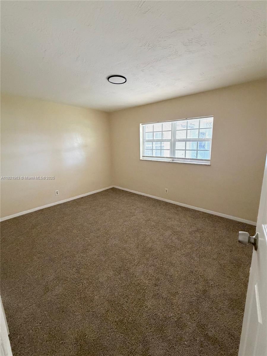 An empty bedroom features beige walls, brown carpeting, and a single window with blinds — 1320 SW 11th Ave # A, Deerfield Beach FL 33441, DEERFIELD BEACH, FL