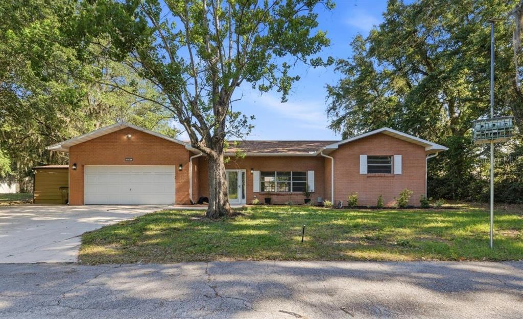 A single-story brick house with a two-car garage and a large tree in the yard — 33201 COVENTRY DRIVE, LEESBURG, FL