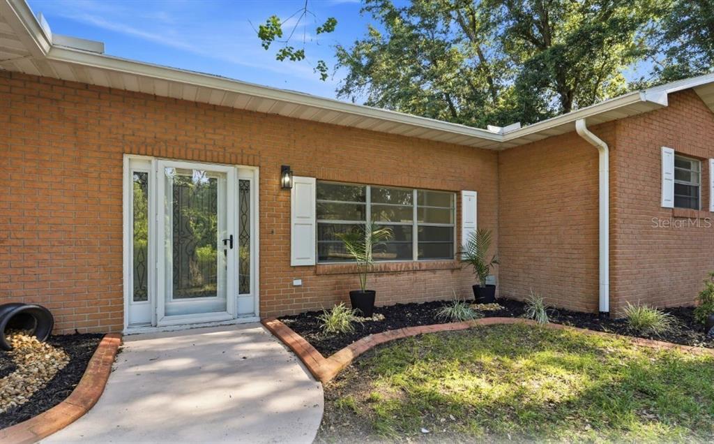 A brick house exterior features a white front door, a large window, and landscaping — 33201 COVENTRY DRIVE, LEESBURG, FL