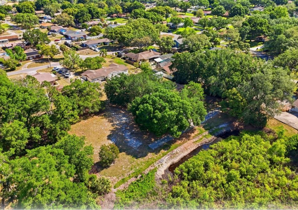 An aerial view shows a vacant, tree-lined lot adjacent to a small canal and neighborhood — 33201 COVENTRY DRIVE, LEESBURG, FL