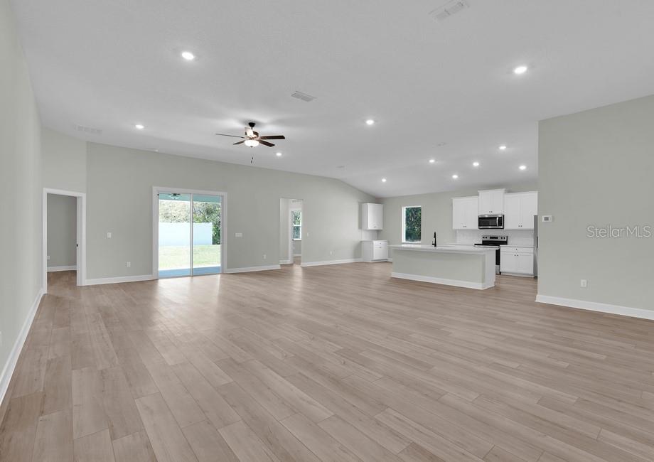 An open-concept living area features light wood-look flooring, a kitchen island, and sliding glass doors — 17399 SW 26TH TERRACE ROAD, OCALA, FL