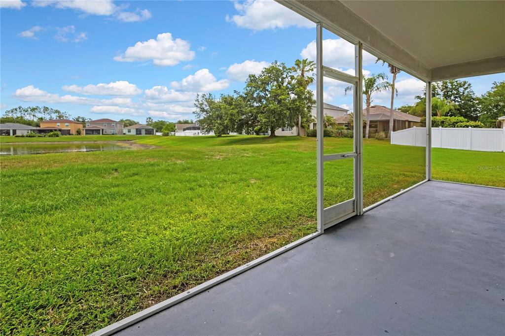 A screened-in patio overlooks a grassy backyard and a small pond under a blue sky — 10536 CORAL KEY AVENUE, TAMPA, FL