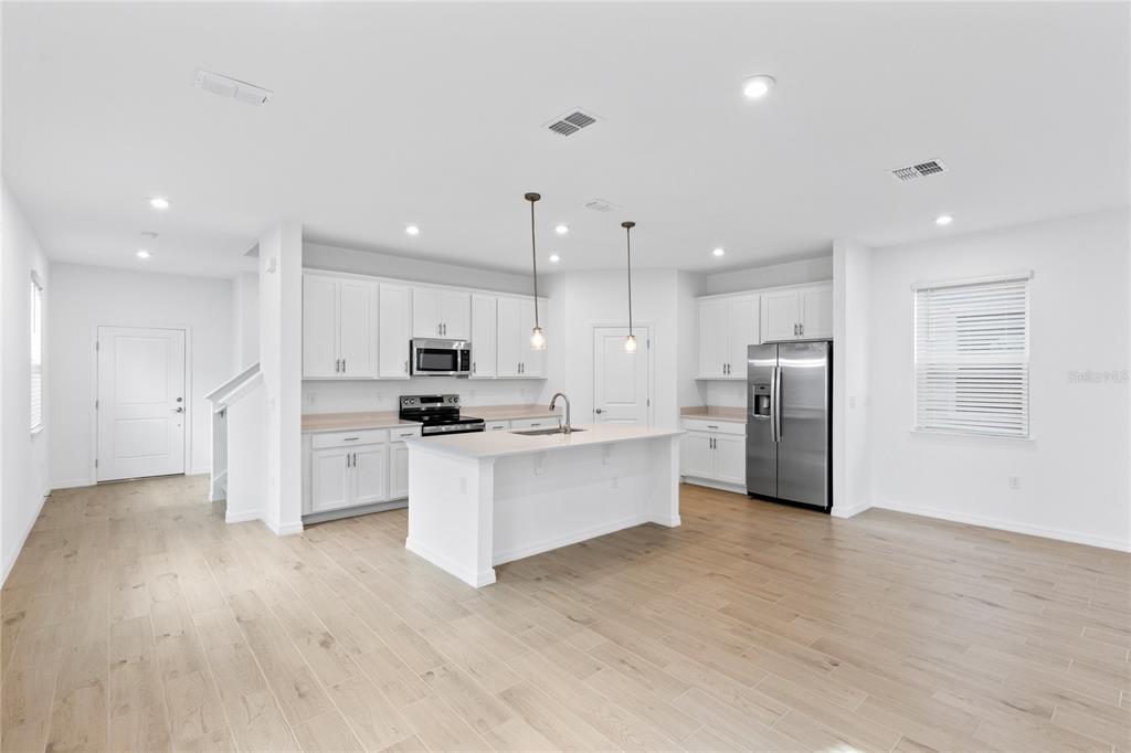 A modern kitchen features white cabinets, stainless steel appliances, a center island, and light wood flooring — 5746 STOCKADE BOULEVARD, ST CLOUD, FL