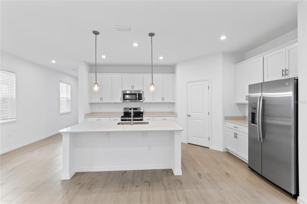 A modern kitchen features white cabinetry, stainless steel appliances, a center island, and light flooring — 5746 STOCKADE BOULEVARD, ST CLOUD, FL