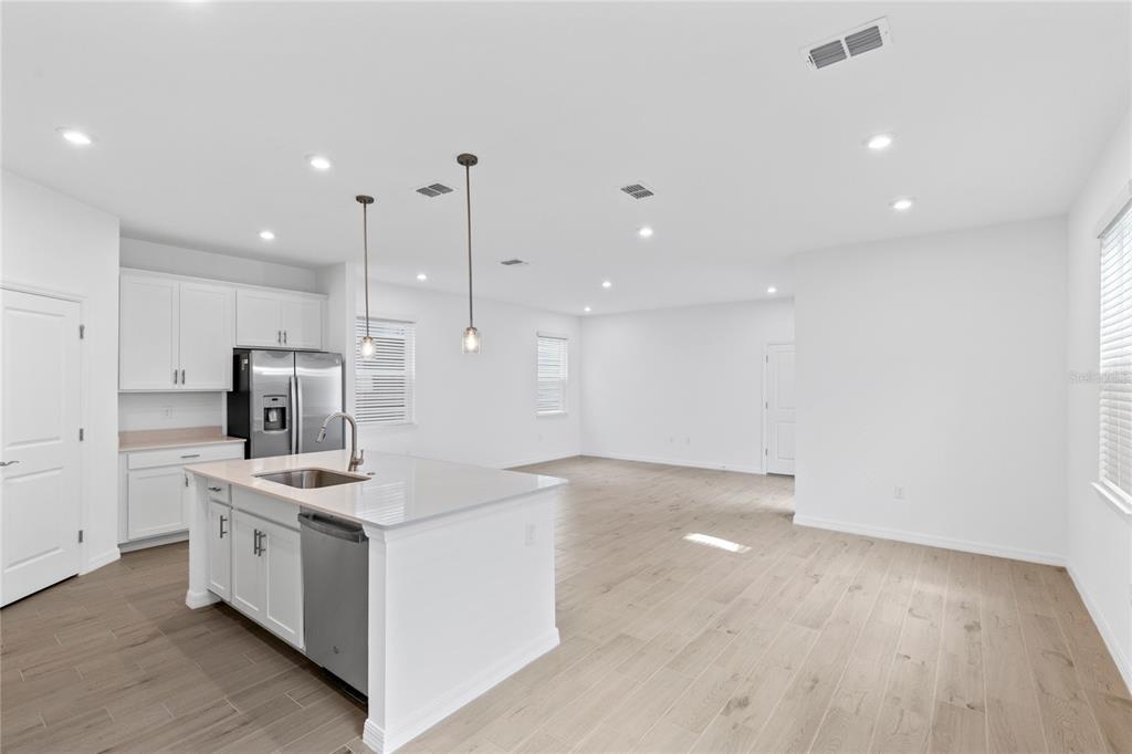 A modern kitchen with white cabinets, a central island, and light wood-look flooring — 5746 STOCKADE BOULEVARD, ST CLOUD, FL