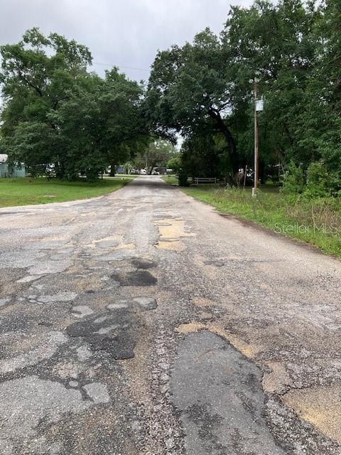 A weathered, unpaved road with numerous patches leads through a tree-lined residential area — SE 21ST PLACE ROAD, SILVER SPRINGS, FL