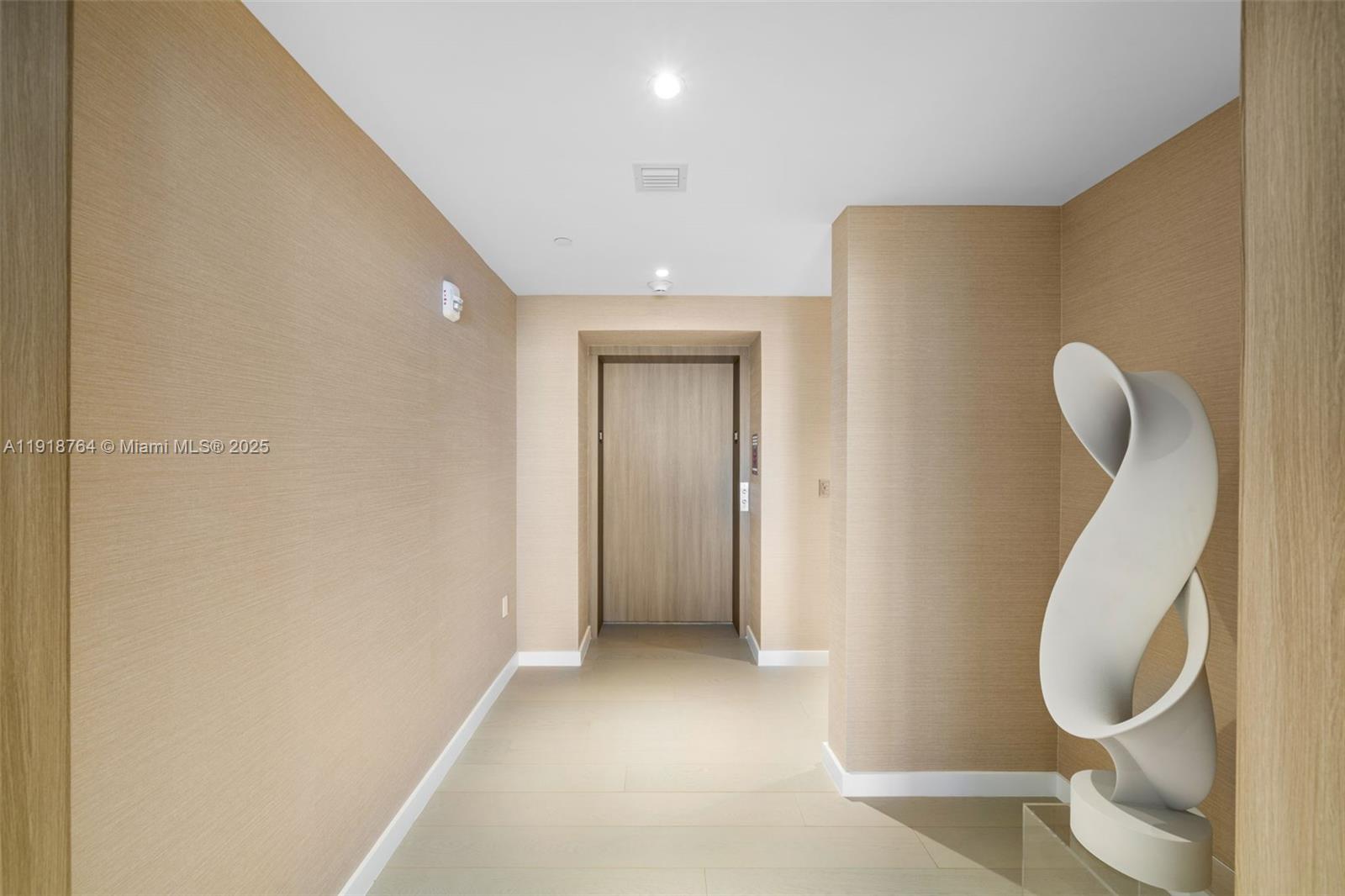 A hallway features textured tan walls, light-colored tile flooring, and a modern white sculpture — 500 Alton, Miami Beach FL 33139, MIAMI BEACH, FL