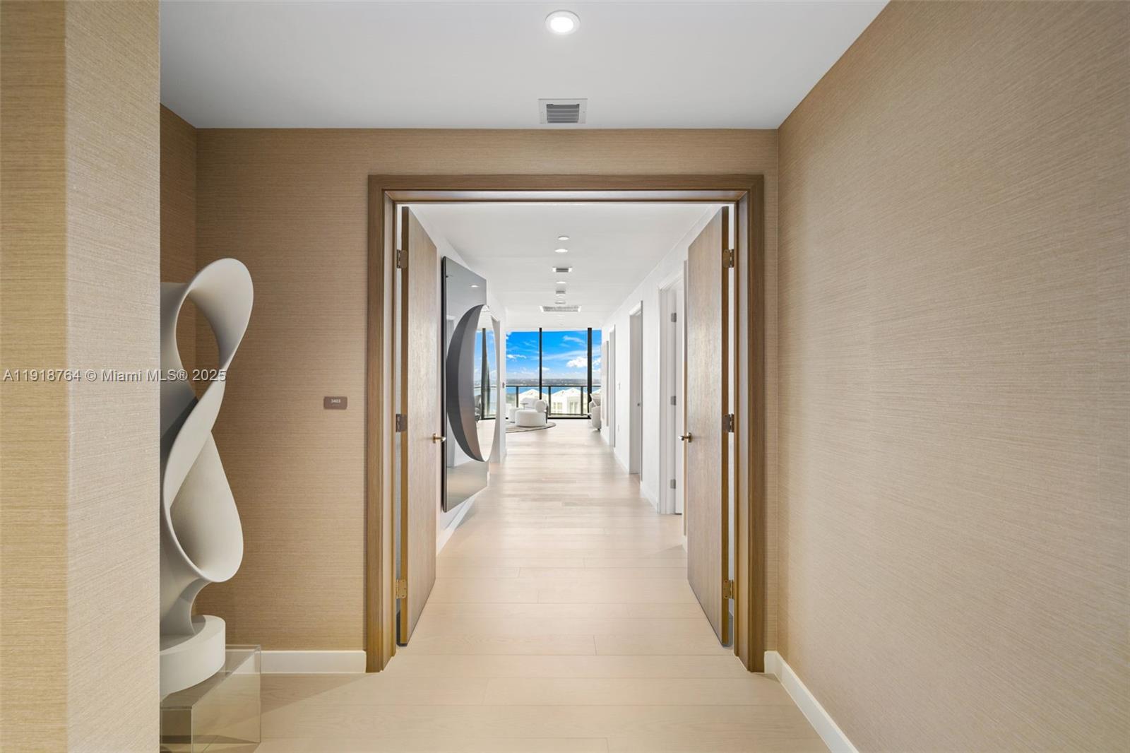 A hallway with light wood flooring leads toward a bright room with floor-to-ceiling windows — 500 Alton, Miami Beach FL 33139, MIAMI BEACH, FL