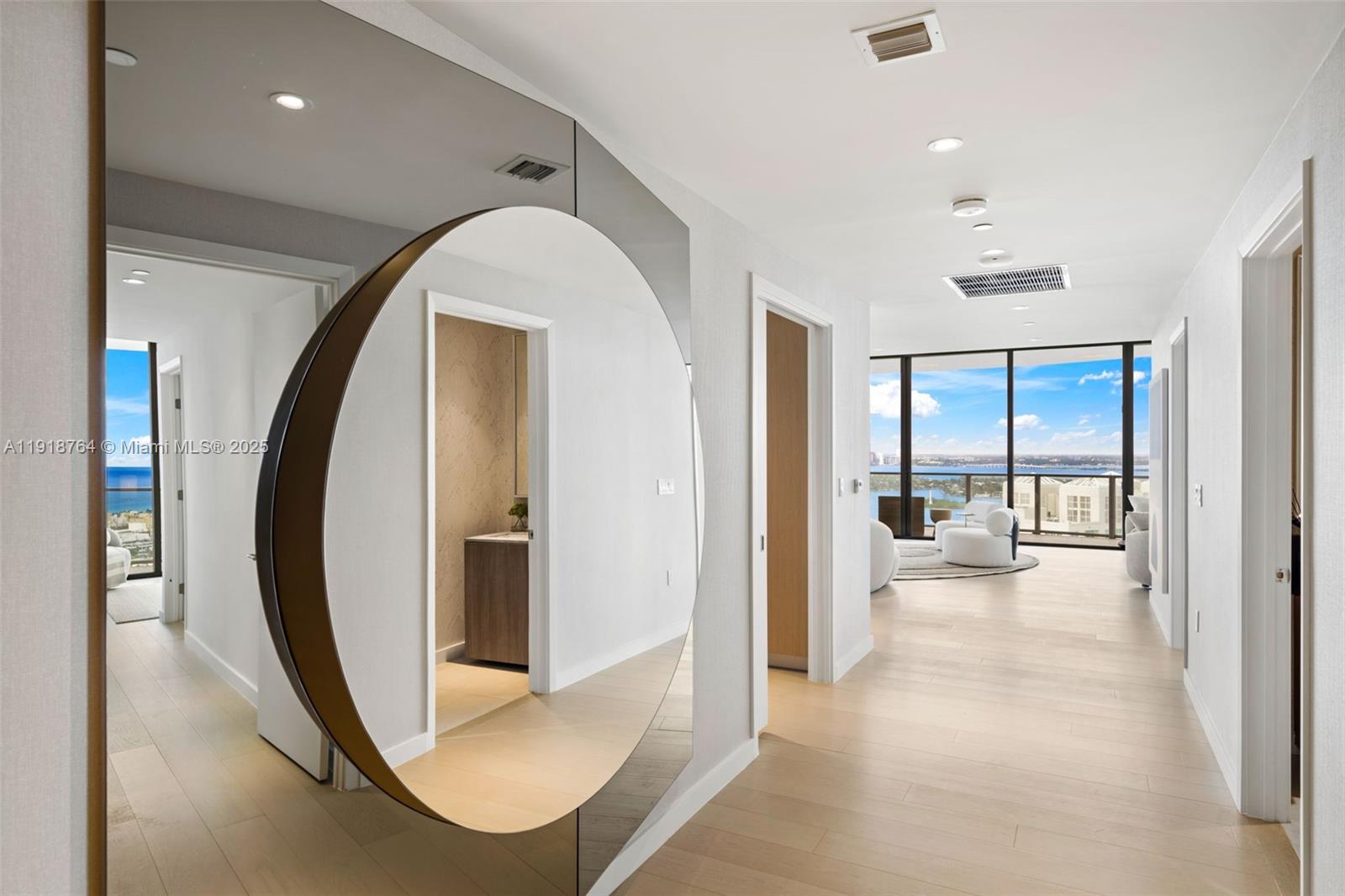 A hallway features light wood flooring, white walls, and a large circular mirror — 500 Alton, Miami Beach FL 33139, MIAMI BEACH, FL
