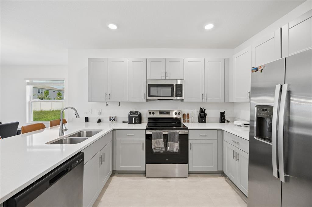 A modern kitchen features light gray cabinets, stainless steel appliances, and white quartz countertops — 5744 LE MARIN WAY, KISSIMMEE, FL