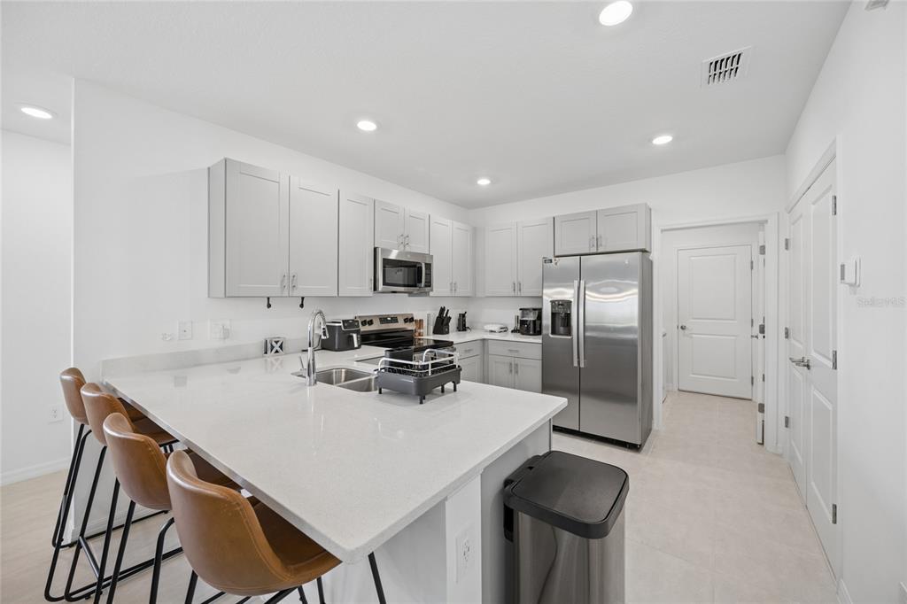 A modern kitchen features white cabinets, stainless steel appliances, and a quartz-topped island with seating — 5744 LE MARIN WAY, KISSIMMEE, FL