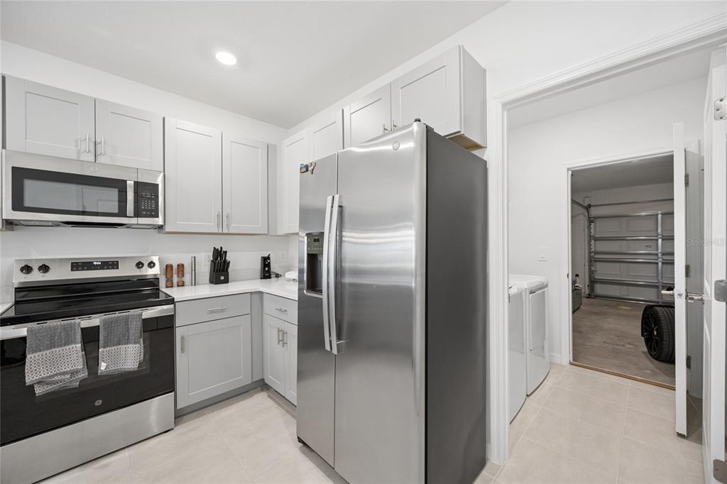 A kitchen with light gray cabinets, stainless steel appliances, and a doorway leading to a garage — 5744 LE MARIN WAY, KISSIMMEE, FL