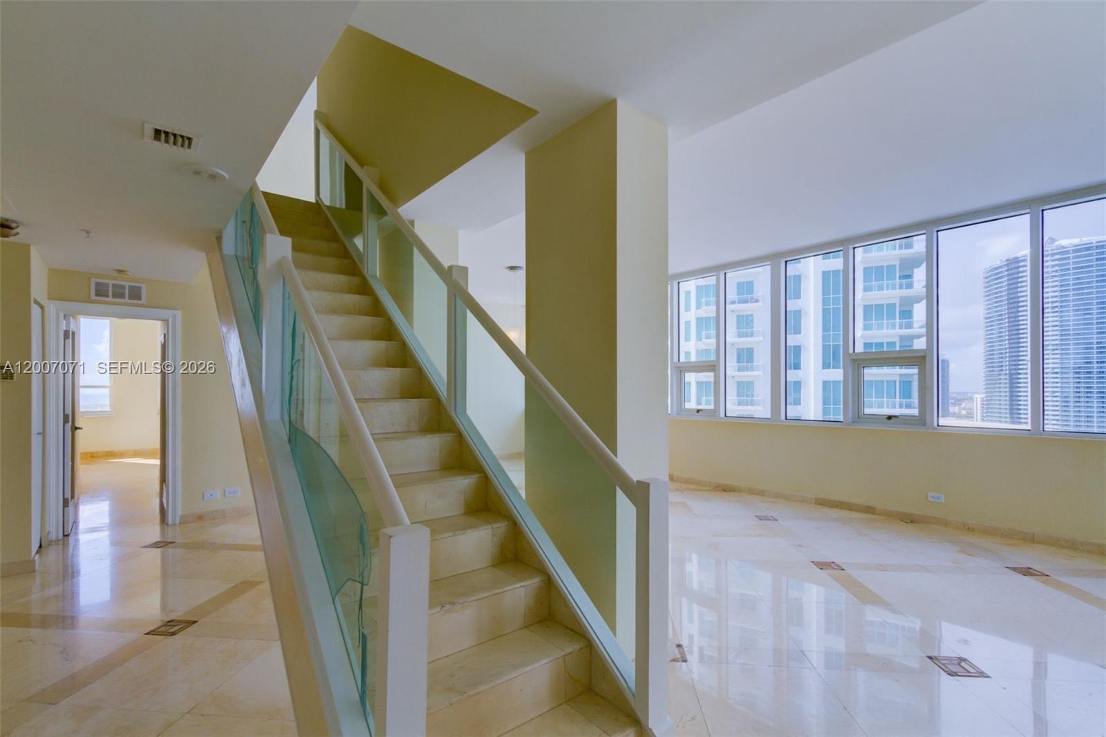 A staircase with glass railings sits in a room with light tile floors and windows — 888 Brickell Key Dr # 2802, Miami FL 33131, MIAMI, FL