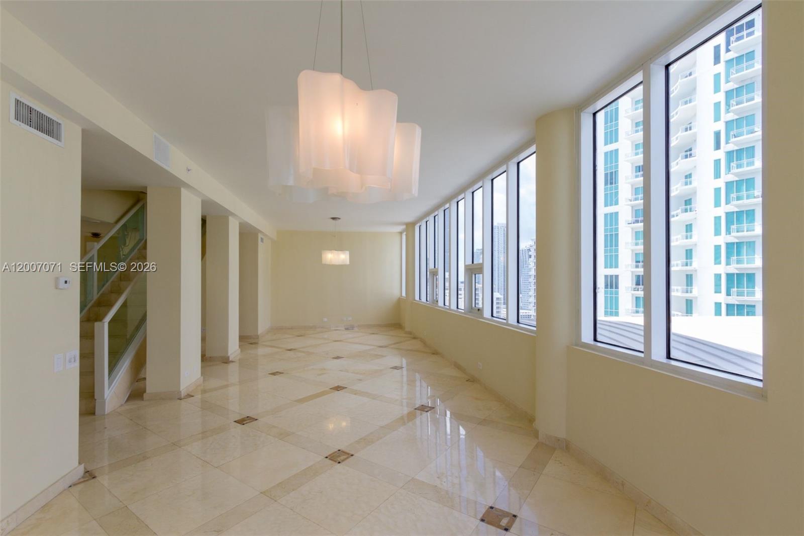 An empty room features light-colored tile floors, large windows, and two modern hanging light fixtures — 888 Brickell Key Dr # 2802, Miami FL 33131, MIAMI, FL