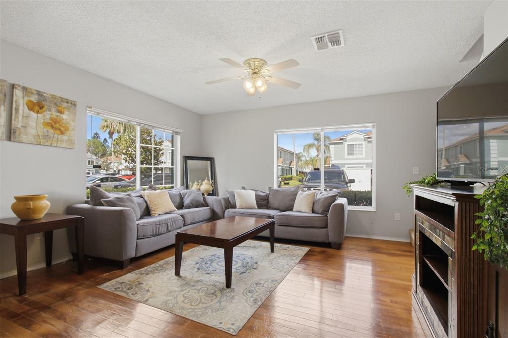 A living room features gray sofas, a wooden coffee table, hardwood floors, and large windows — 1328 TWILRIDGE PLACE, BRANDON, FL
