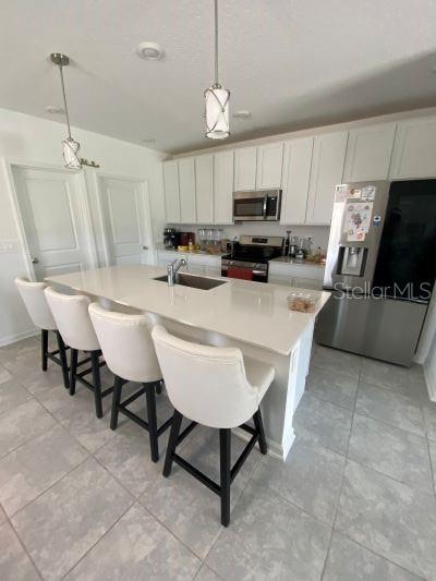 A kitchen with white cabinets, a quartz-topped island, four bar stools, and stainless steel appliances — 4258 TWISTED TWIG BEND, KISSIMMEE, FL