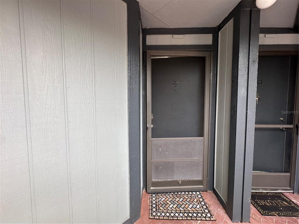 A dark-colored front door with a screen door is set between gray paneled exterior walls — 3766 SOUTHPOINTE DRIVE UNIT U5, ORLANDO, FL